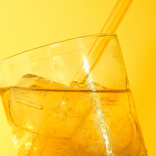 Lemonade and iced tea cocktail with ice and a straw with a yellow background