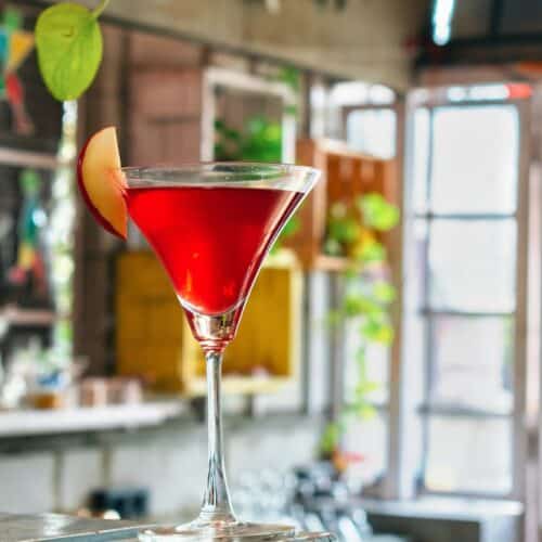 martini glass with red liquid and sliced apple