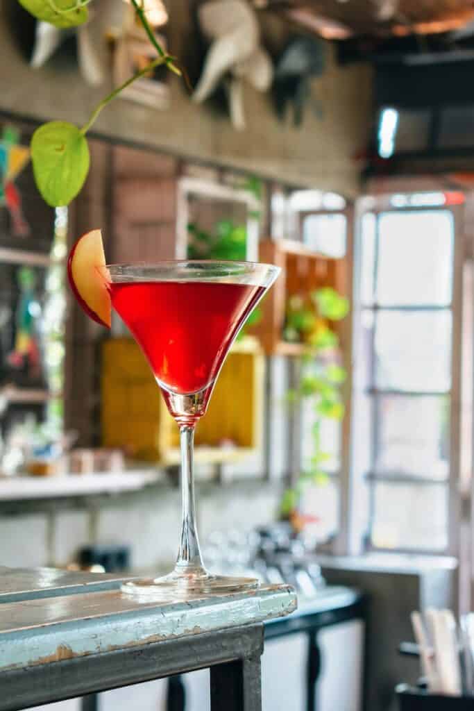 martini glass with red liquid and sliced apple