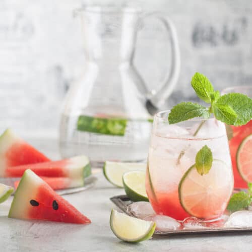 A glass with lemonade and watermelon juice with a lime and a sprig of mint for garnish