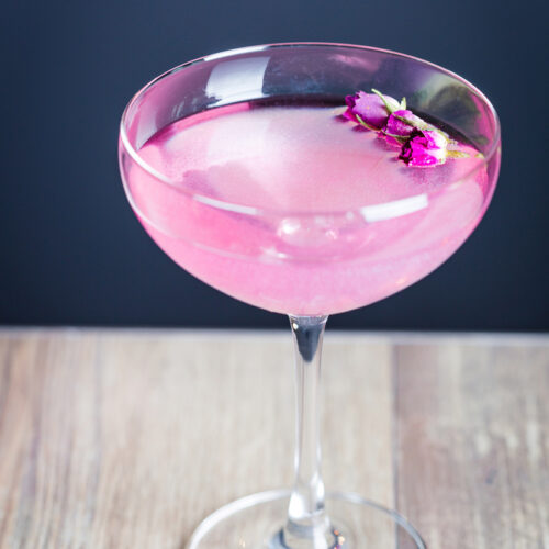 Pink cocktail with flowers as garnish in a coupe glass