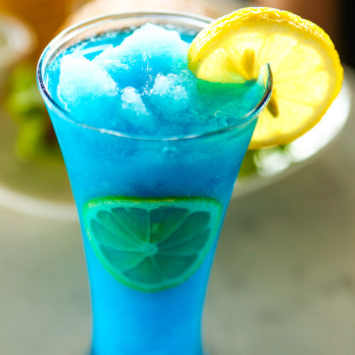 Blue frozen cocktail in a tall glass with a lemon garnish