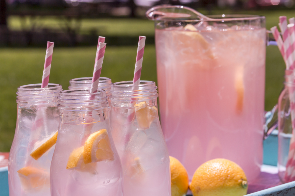 4 small glass bottles and pitcher filled with fresh squeezed Rose Lemon Spritzers with pink swirled straws and lemon slices