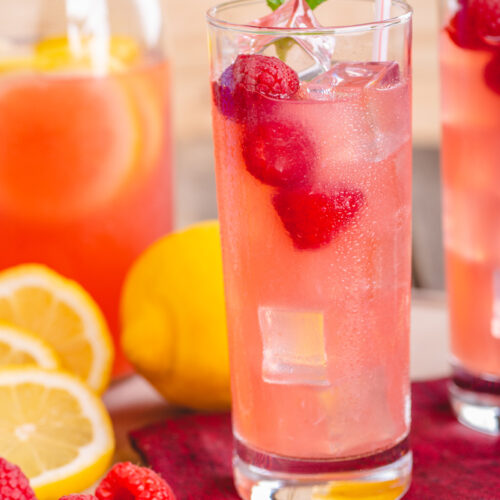 A glass of sparkling raspberry lemonade with raspberries in glass and sliced lemon on table