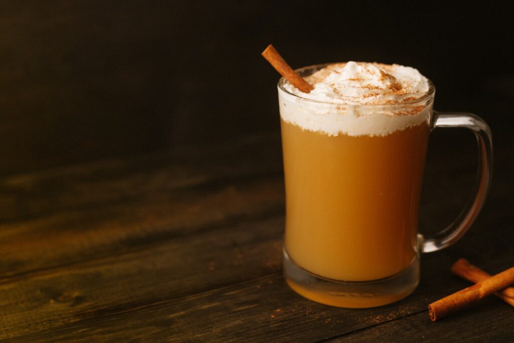 Warm cider with cream on top and cinnamon stick