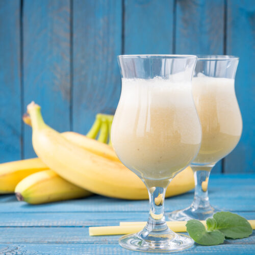 Banana Daiquiri in a glass with bananas behind it on a blue wooden background