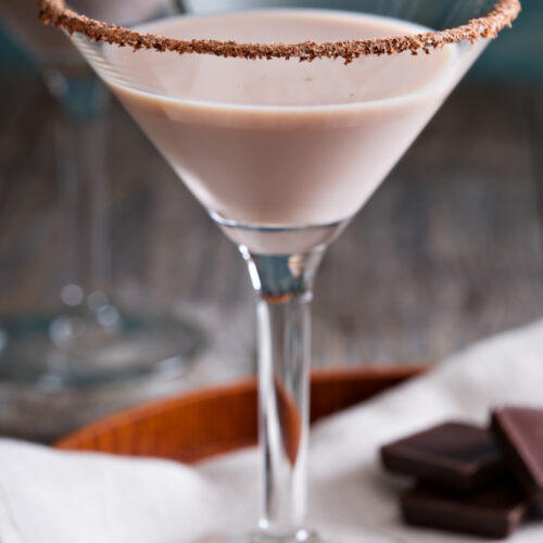 A chocolate martini in a martini glass with chocolates in the background