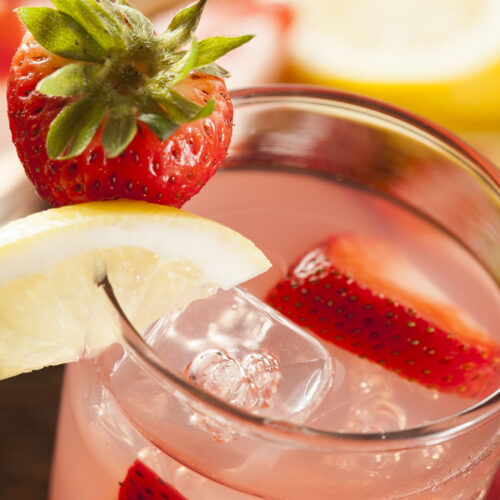 Strawberry Lemonade in a glass with a lemon and strawberry garnish on rim