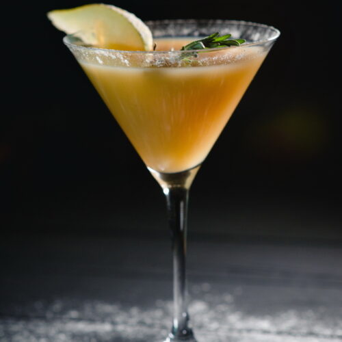 Cinnamon Pear Margarita in a Martini glass with a slice of pear as garnish on a black table with white powder splashed across