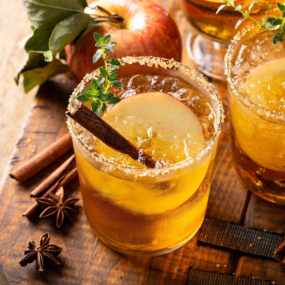 Spiced apple Margarita in a rocks glass with a stick of cinnamon and apples in the background