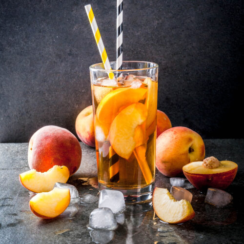 Peach cocktail made with unsweetened tea and peaches in a glass with straws