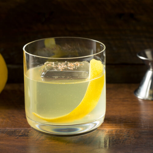 Clarified Whiskey Sour in a glass with a large ice cube and a slice of lemon peel