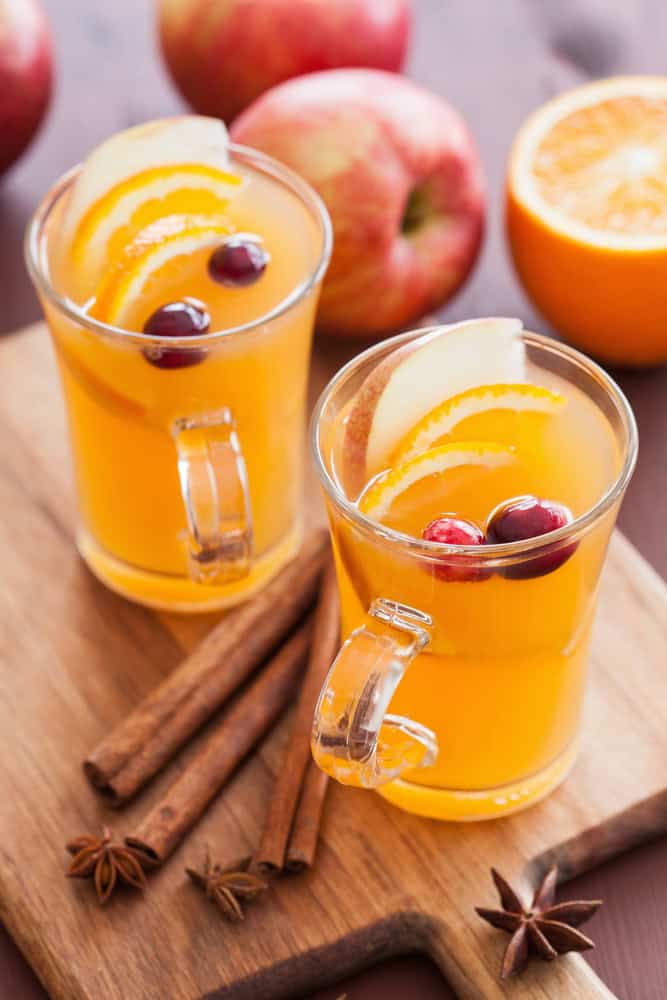 Non-Alcoholic Holiday Punch in two glasses with apples, oranges and cranberries for garnish on a cutting board