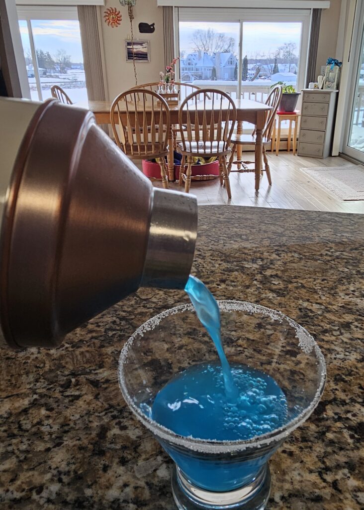 Cocktail Shaker pouring a Honolulu Blue Lions Kool-Aid Martini into a Martini glass
