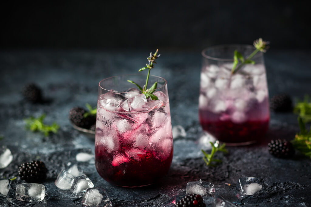 Two glasses of blackberry lemonade with sprigs of Rosemary and blackberries on the table