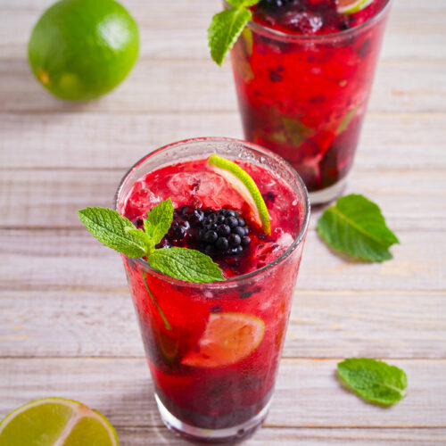 Blackberry Basil Mojito in two glasses with lime and basil on a table.