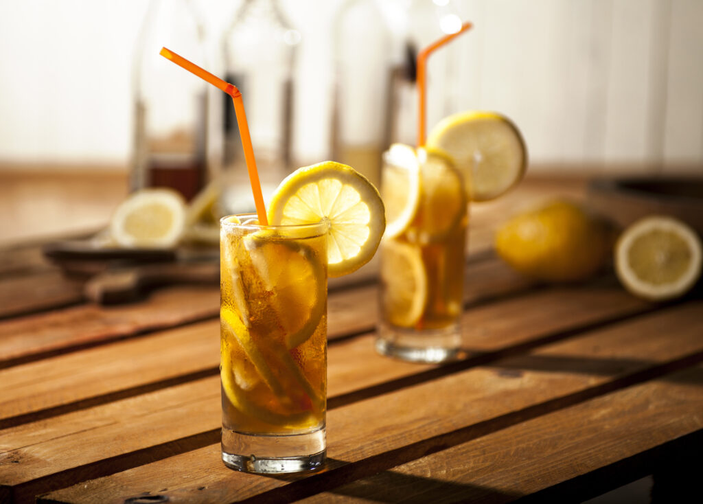 Perfect Long Island Iced Tea on a wooden table with lemon slices and a straw