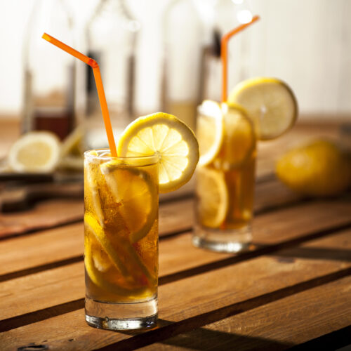 Perfect Long Island Iced Tea on a wooden table with lemon slices and a straw