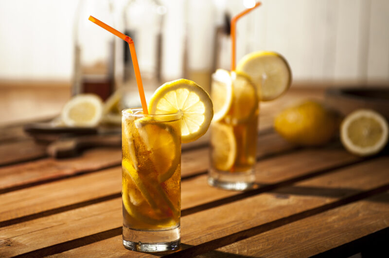 Perfect Long Island Iced Tea on a wooden table with lemon slices and a straw