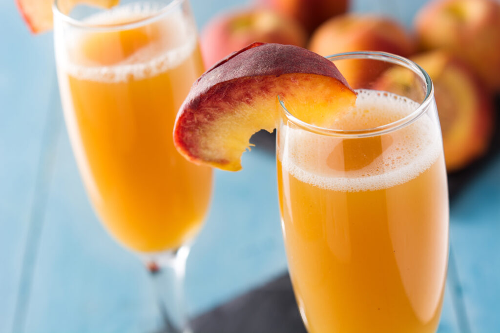 Mimosa Bar favorite Peach Bellini in a champagne flute with a piece of peach on the edge