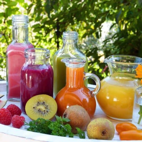 Fruit Smoothies with sliced fruit in front of pitchers.