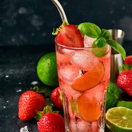 A Collins glass filled with Gin and Tonic, strawberries and lime with a straw and ice