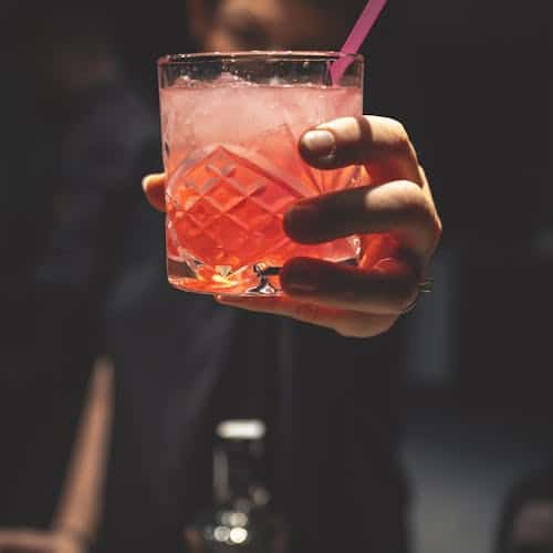 Man Holding Forward A Glass Of Rum Punch With A Straw