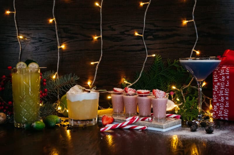 4 different cocktails with white twinkle lights in the background and Christmas decorations