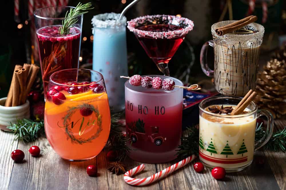 Christmas Cocktail Bar with seven Cocktail glasses with different drinks inside and random Christmas decorations.