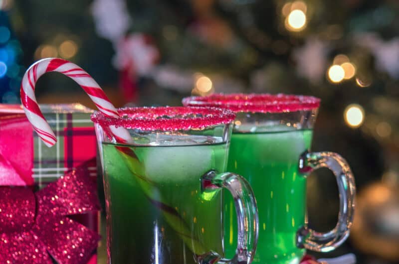 Grinch Mocktail Punch - green liquid in a glass with a candy cane garnish and red candy rim