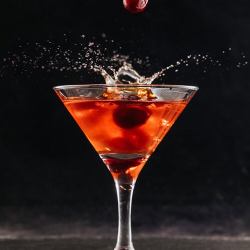 Arrowhead Red Cocktail with cherries splashing into martini glass