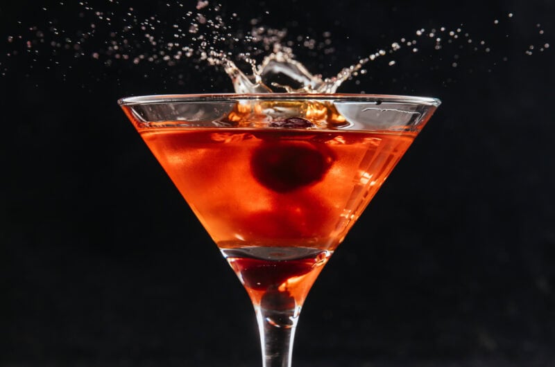 Arrowhead Red Cocktail with cherries splashing into martini glass