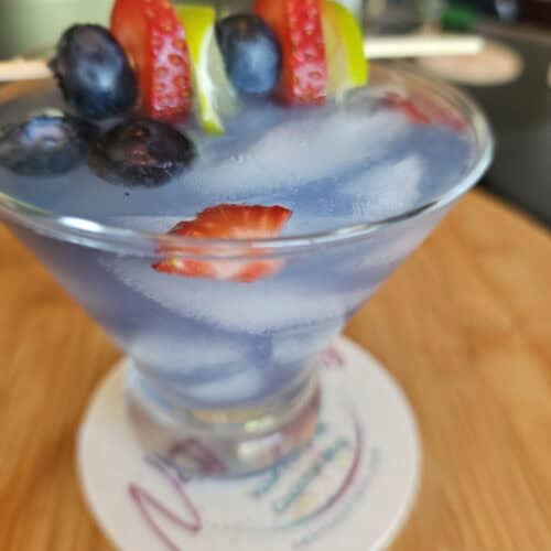 A Blue Berry Electric Cocktail with a garnish of Strawberries, Blueberries and limes.