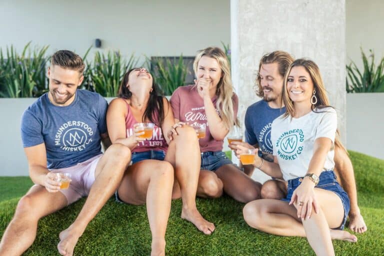a group of people sitting on top of a lush green field enjoying a cocktail