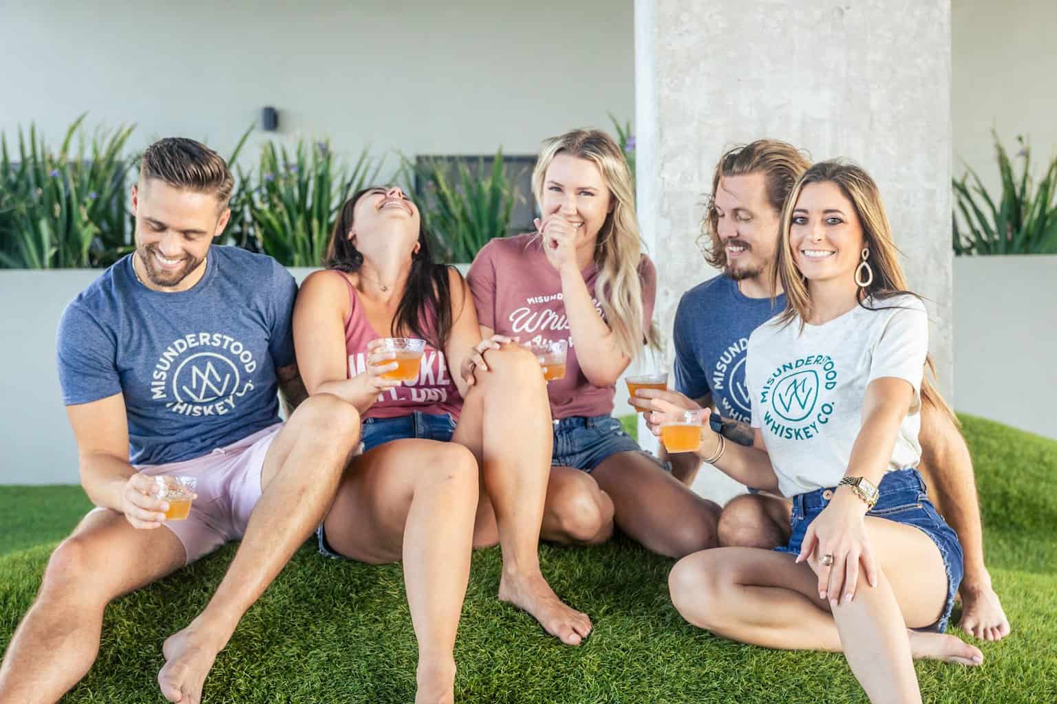 a group of people sitting on top of a lush green field enjoying a cocktail