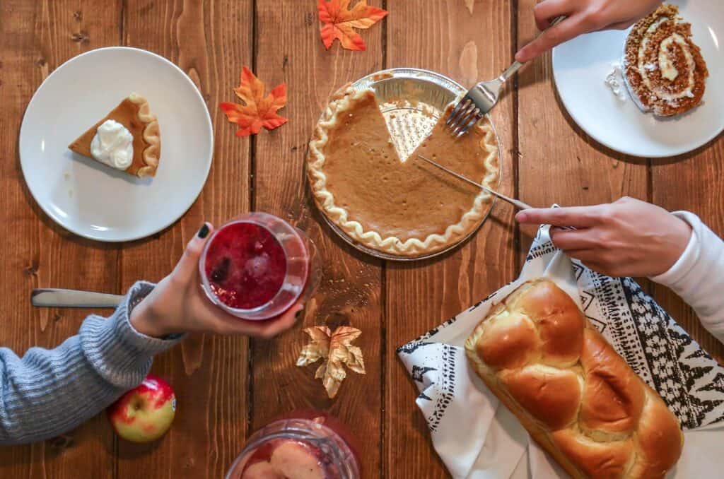 person slicing pie beside bread and a cocktail