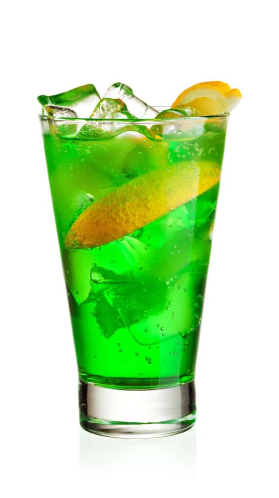Bright green Mary Jane Punch Cocktail with an orange slice and ice in a glass