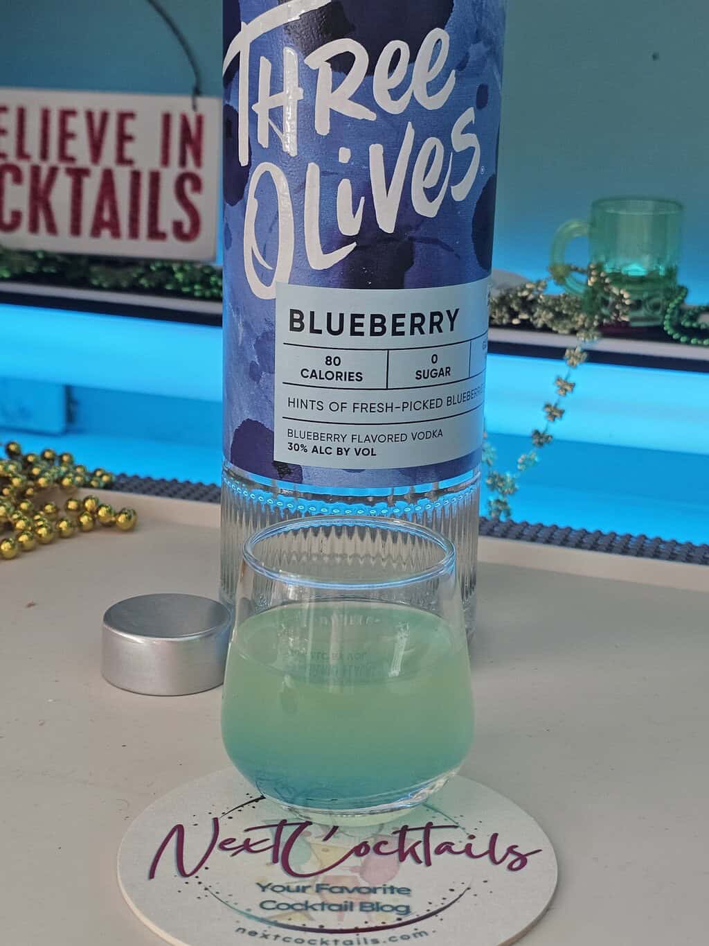 Cocktail shot with a bottle of blueberry vodka behind it