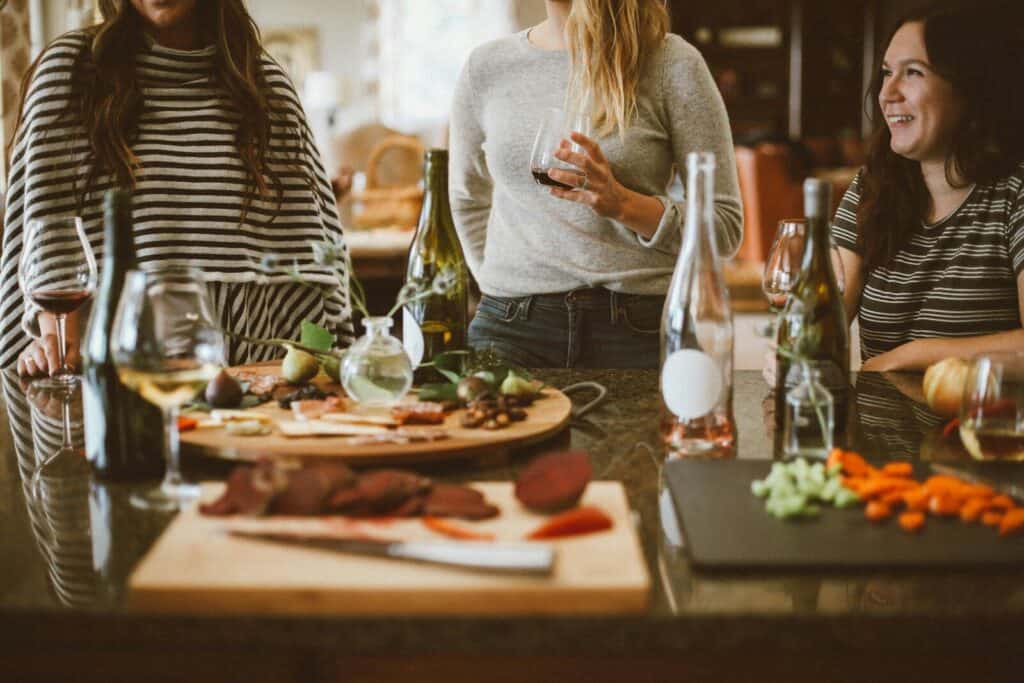two woman standing beside woman sitting in front of table with appetizers