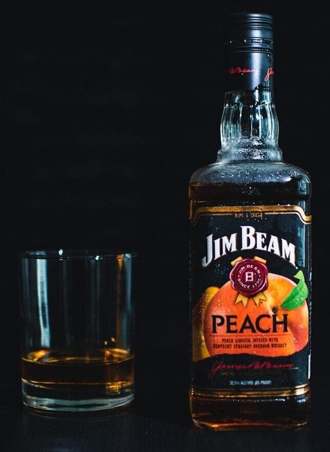 Jim Beam Peach Whiskey bottle beside a glass with a shot of the liquor