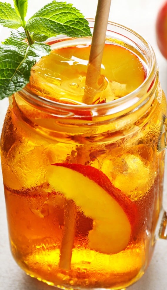 A mason jar filled with peach whiskey lemonade, ice and slices of peach with a straw