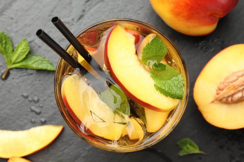 A view of peach whiskey lemonade from the top with sliced peaches and two straws